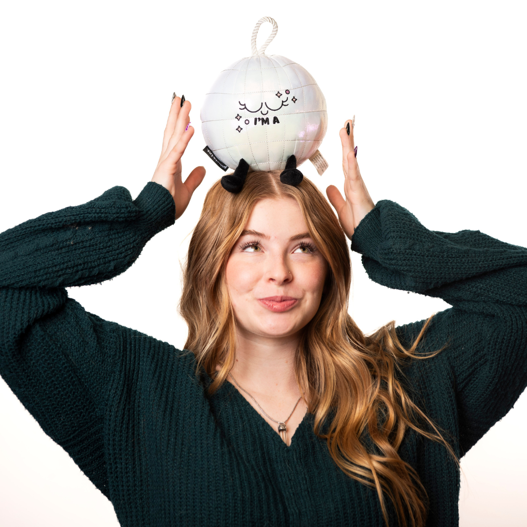 A model holding a plush resembling a disco ball with a silver body, black legs, and a face expressing surprise or excitement with the text 'I'M A' on it.