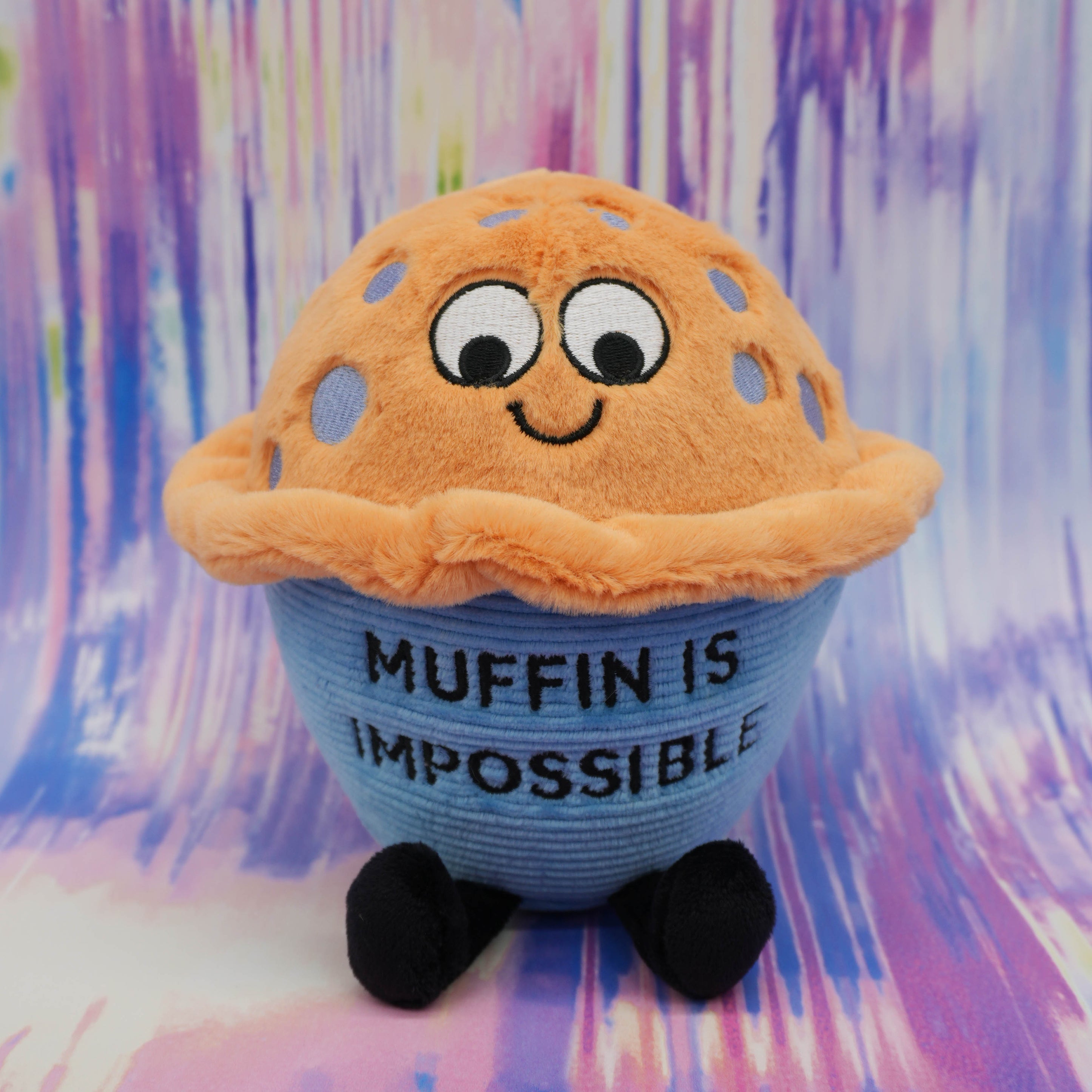 Plush toy resembling a muffin with text muffin is impossible written on it on a colorful background