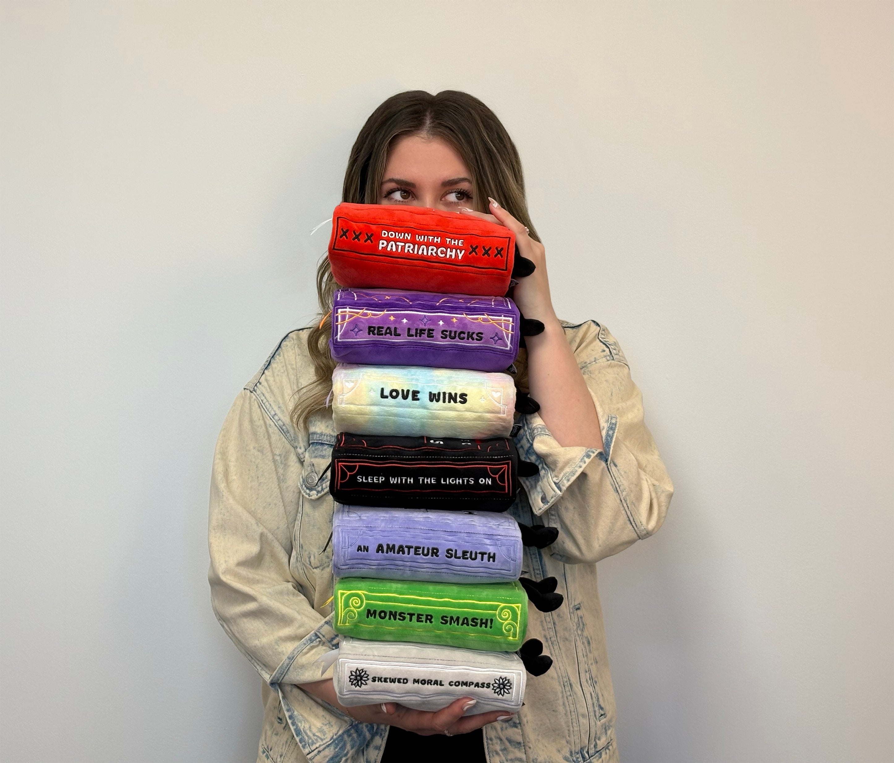 Woman holding a stack of colorful books of several genres on a plain background