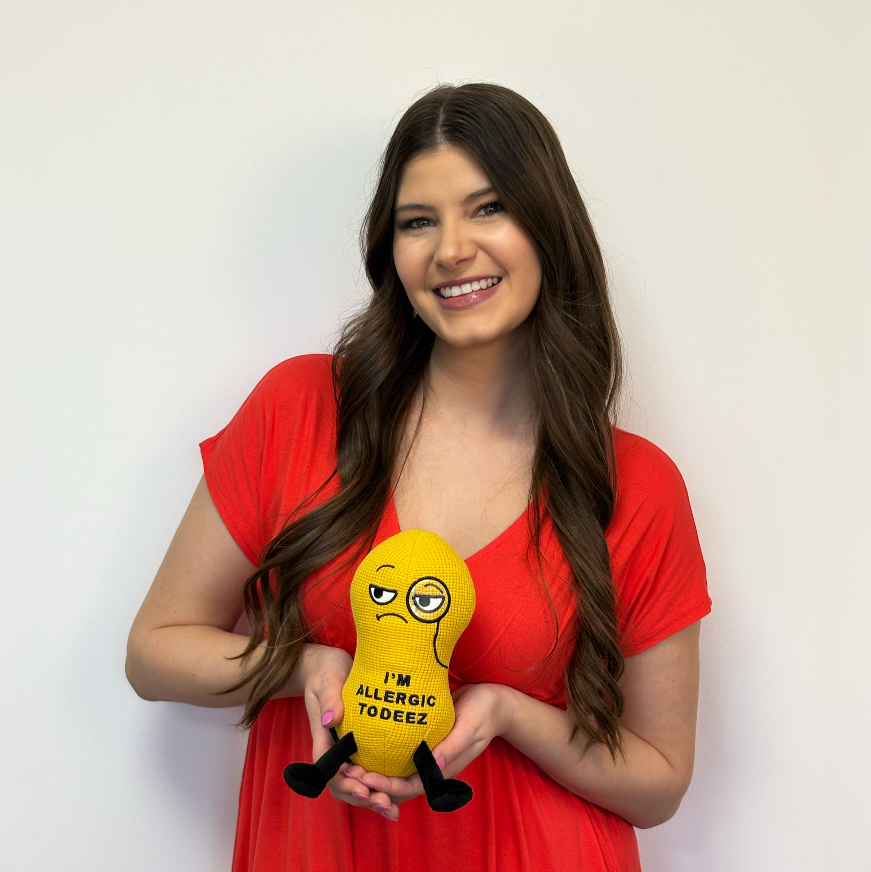 Woman in a red dress holding a peanut plush that reads, 'I'm allergic to deez.'