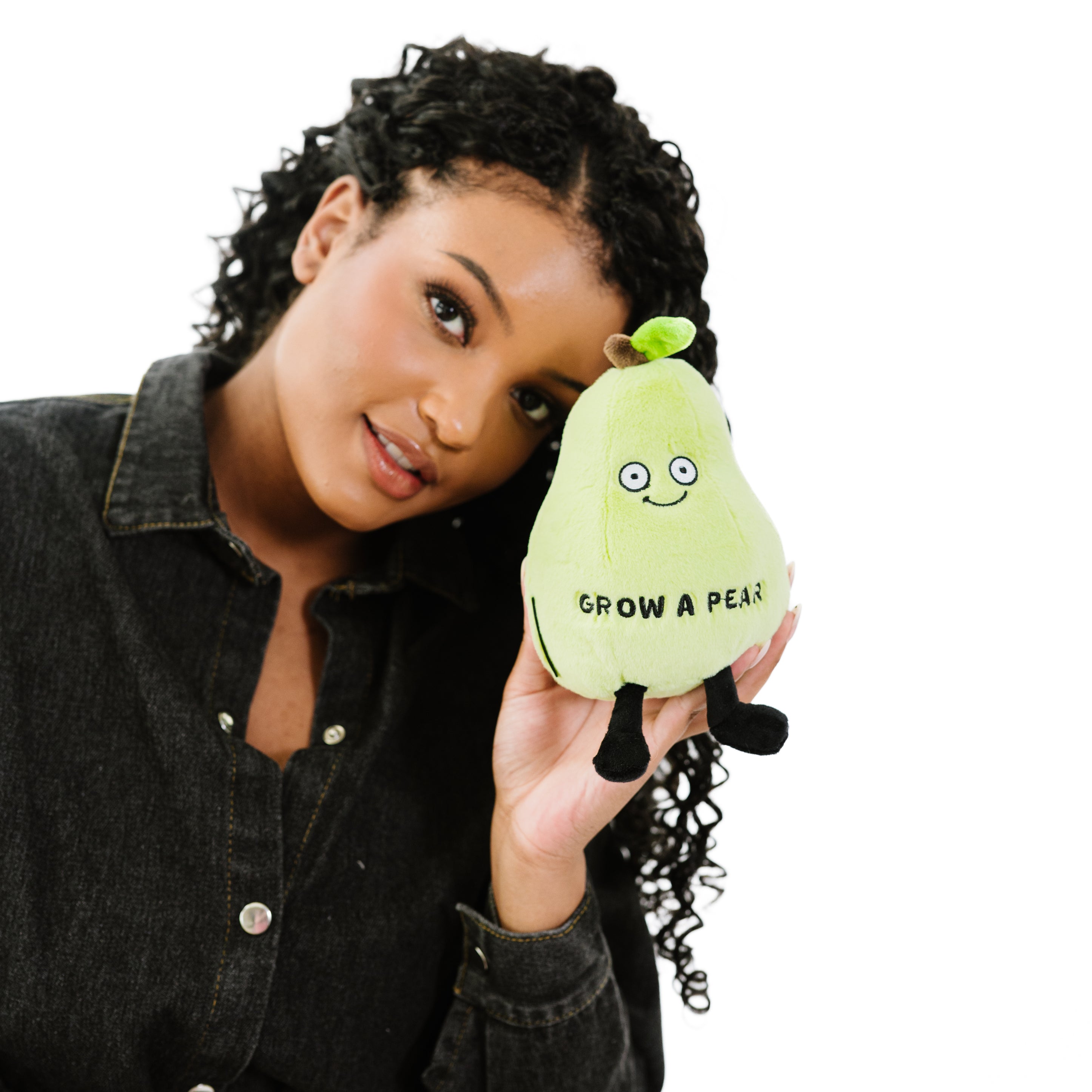 A woman holding a plush shaped like a green pear featuring a smiling face and the text 'GROW A PEAR'written on it