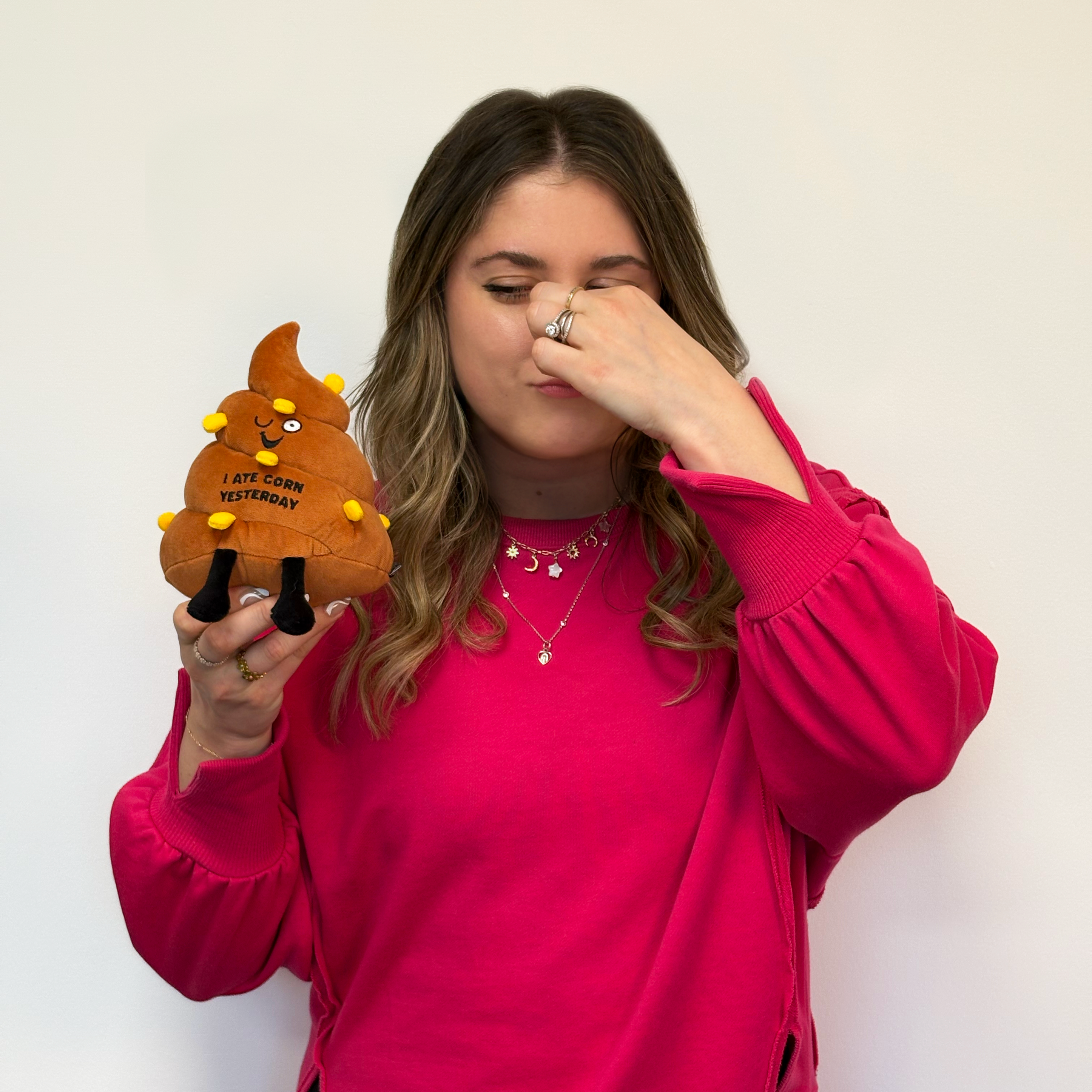 Woman holding a poop plush with 3D corn pieces that reads, 'I ate corn yesterday.'