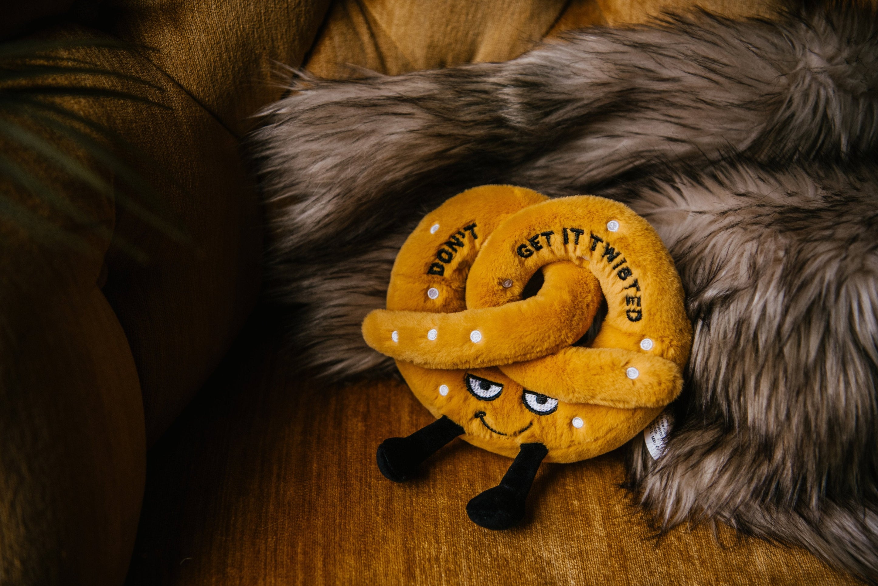 A plush designed to look like a twisted pretzel with the text 'Don't get it twisted' written on it placed on a couch.