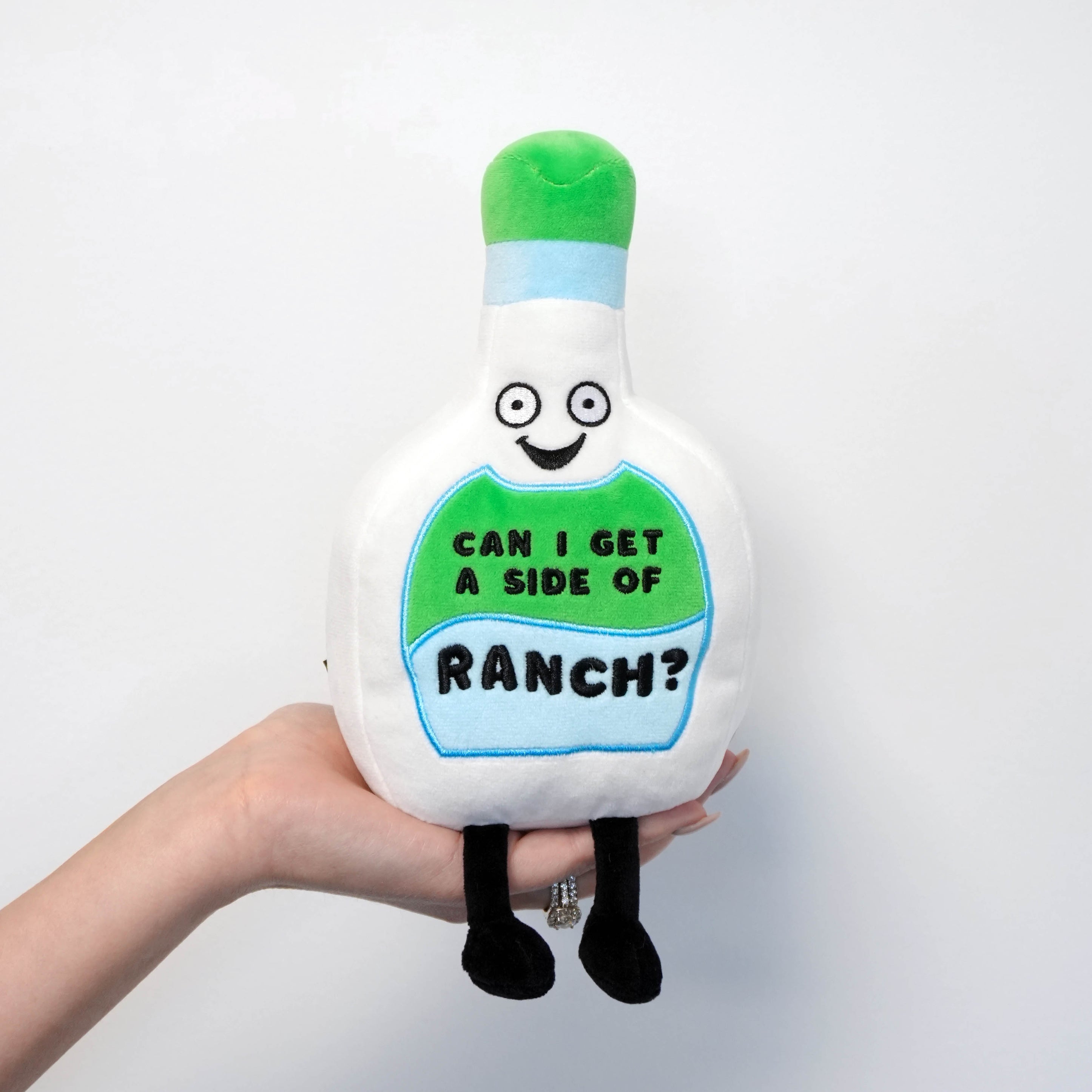 Plush toy resembling a bottle of ranch dressing with text 'Can I get a side of ranch?' held by a hand against a white background.