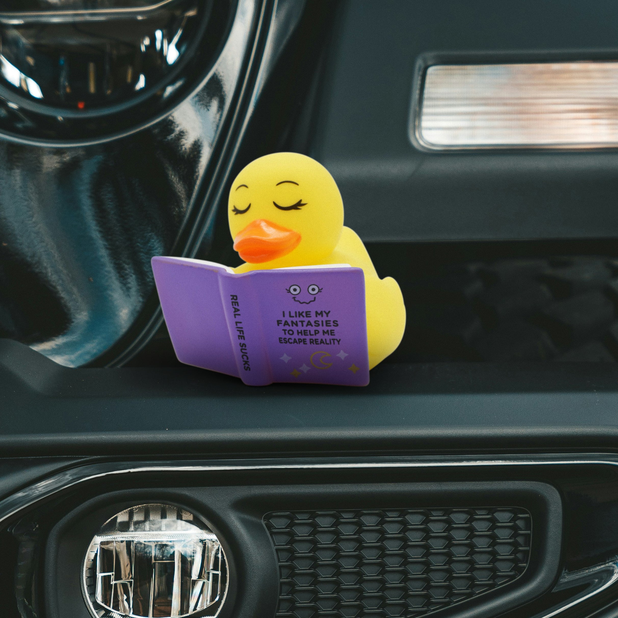 Yellow rubber duck reading a fantasy book on a car dashboard
