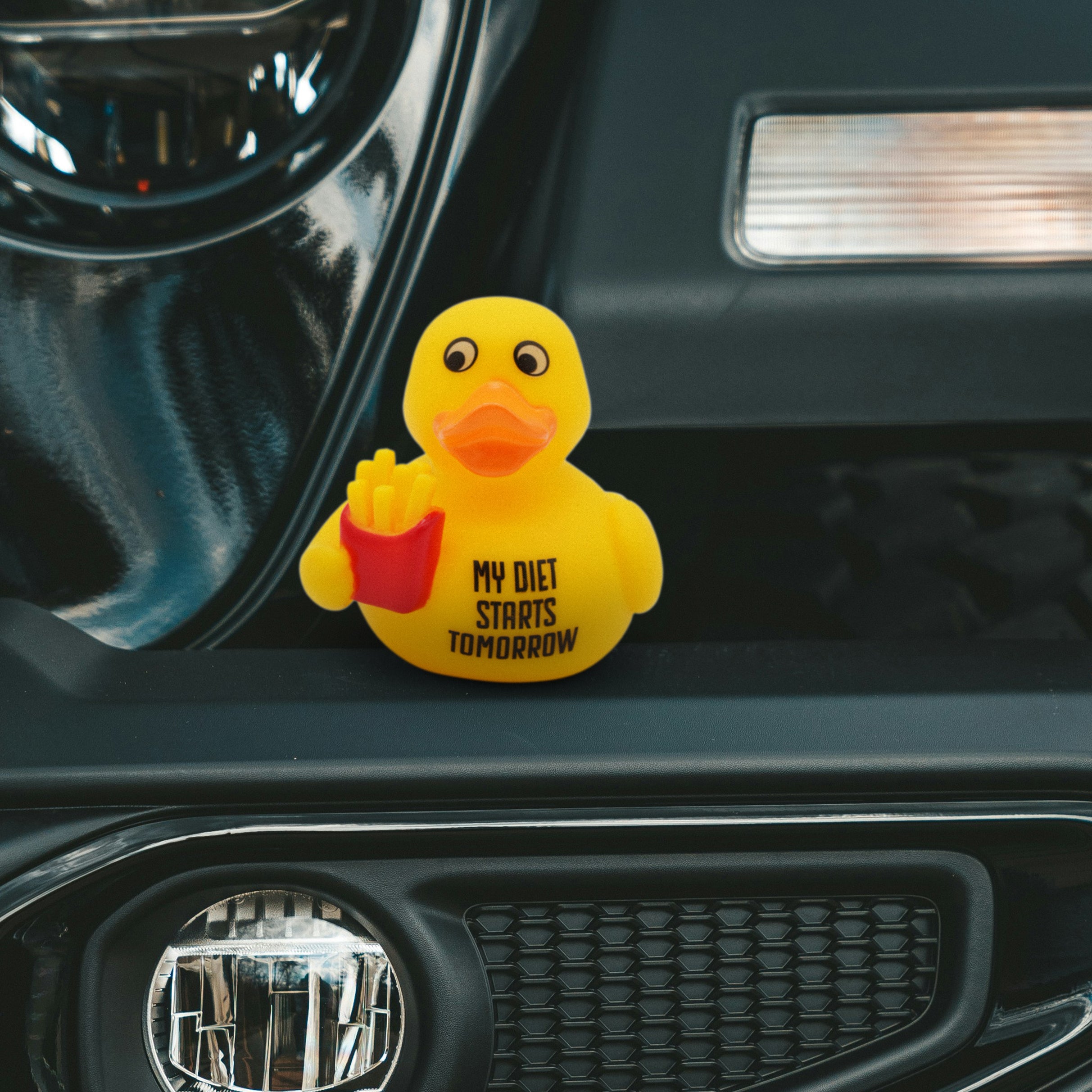 Yellow rubber duck holding fries with 'My Diet Starts Tomorrow' text on a car dashboard.