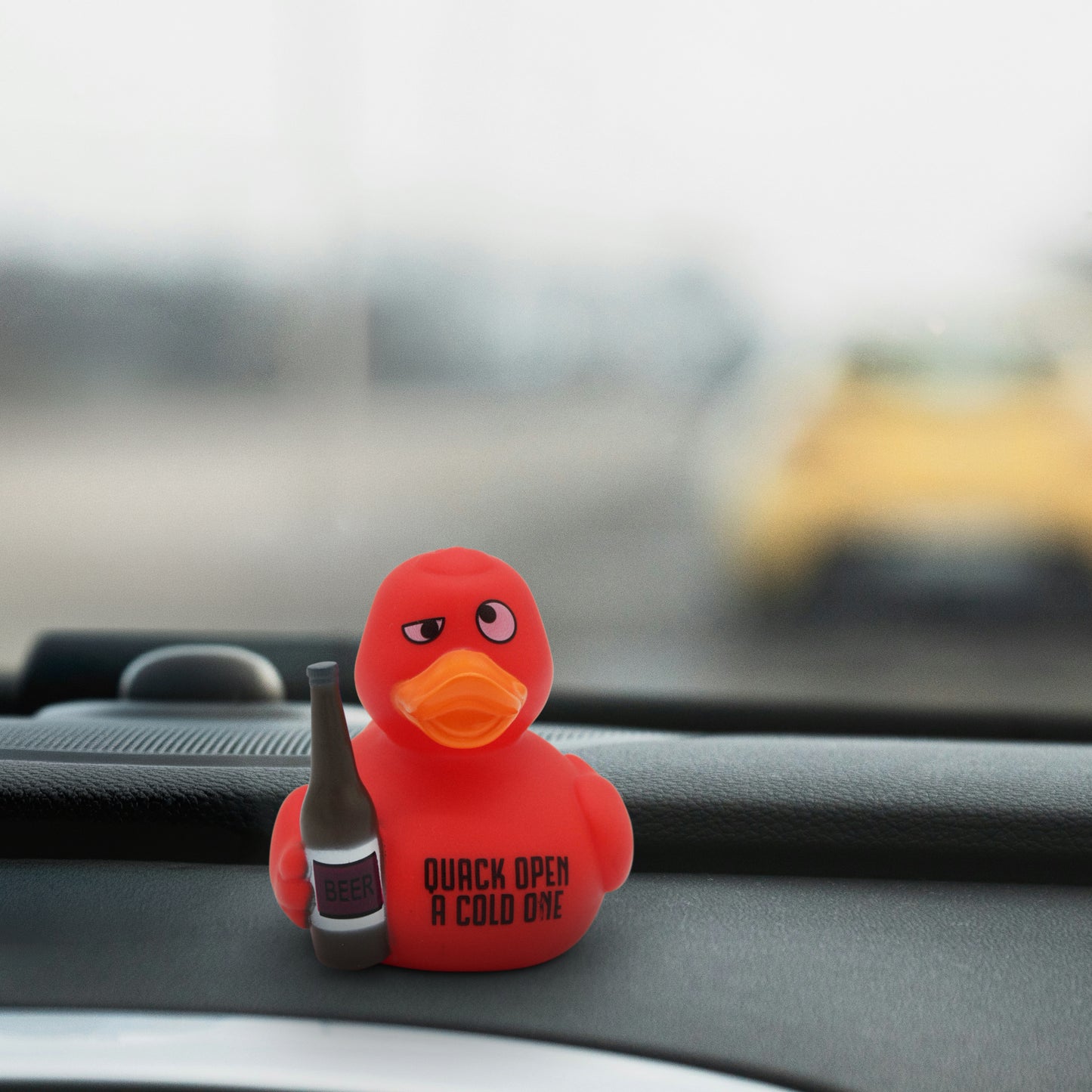 Red rubber duck holding a beer bottle with 'Quack Open A Cold One' text on a car dashboard