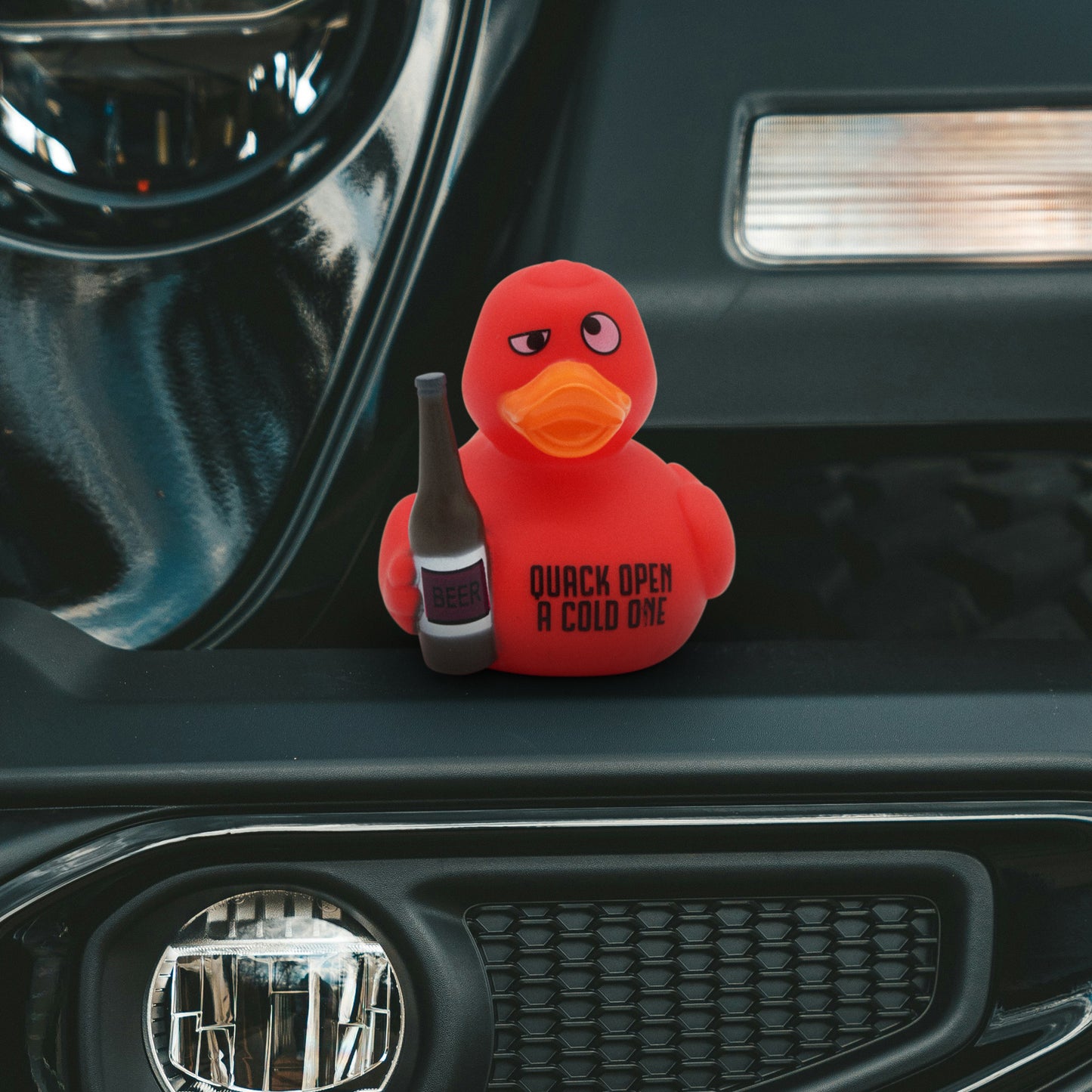 Red rubber duck holding a beer bottle with 'Quack Open A Cold One' text on a car dashboard