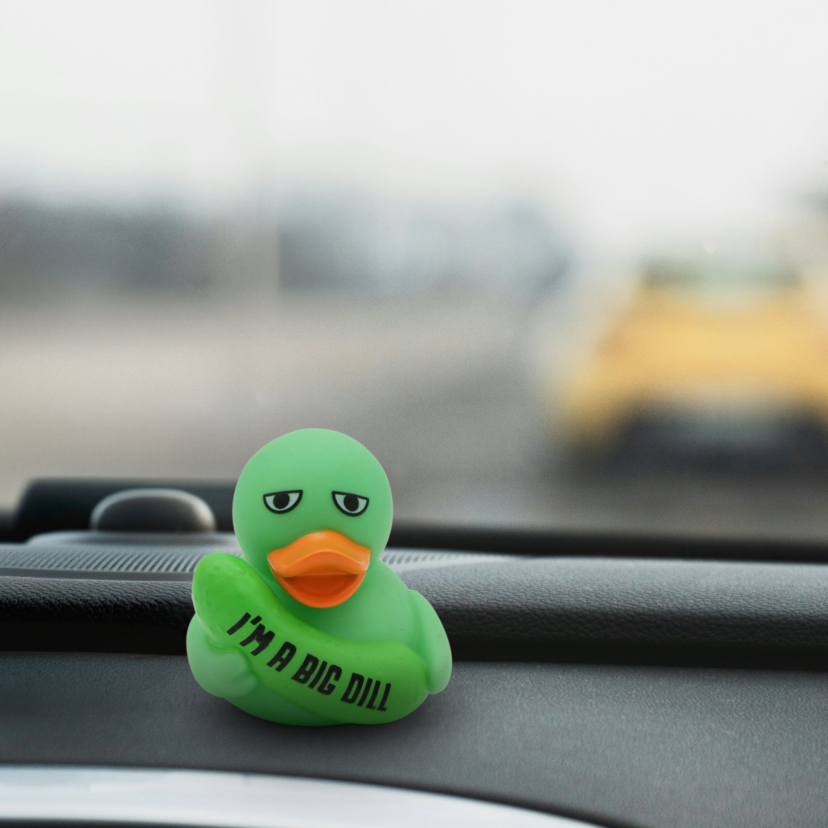 Green rubber duck holding a pickle with 'I'm a Big Dill' text on a car dashboard