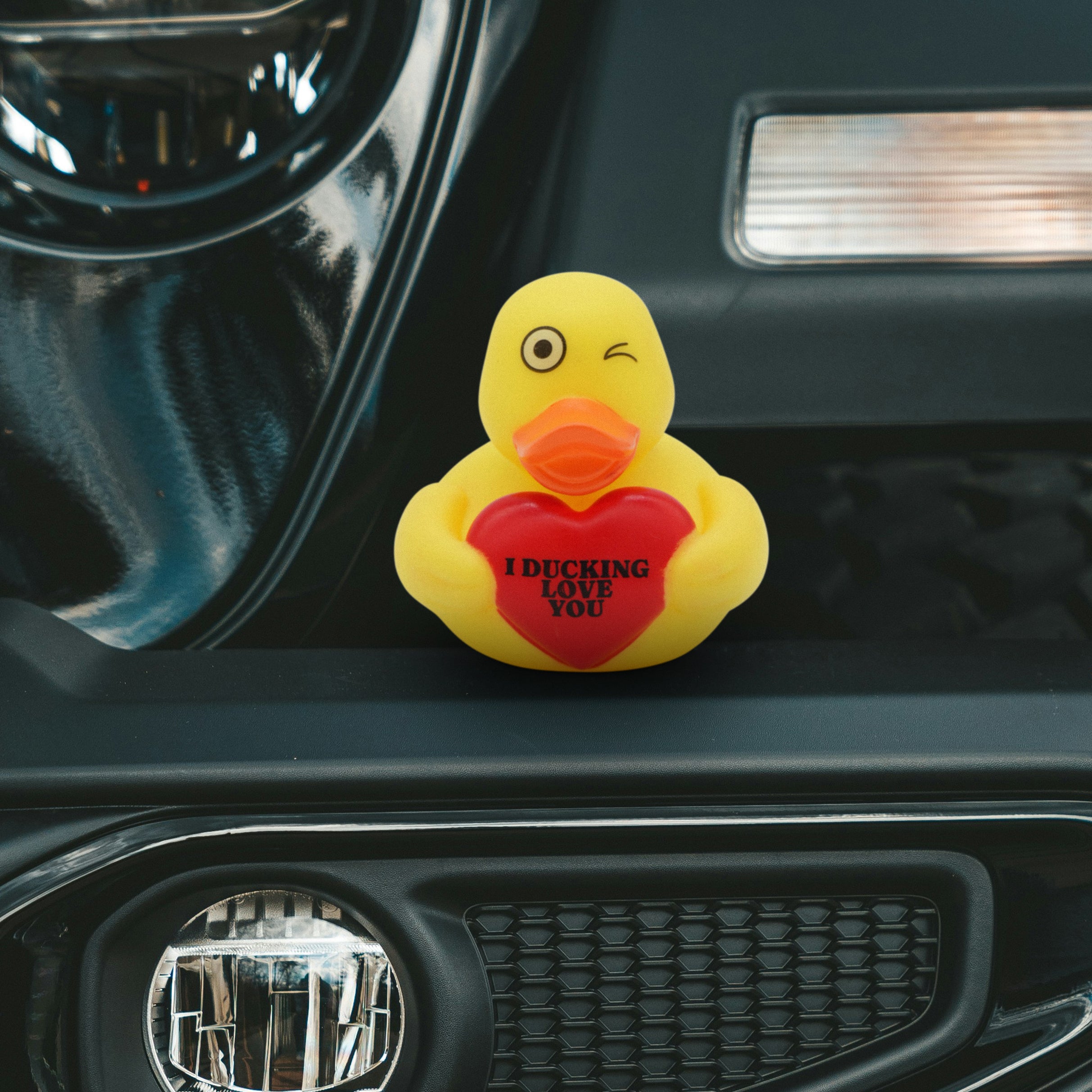 Yellow rubber duck with a red heart that reads "I ducking love you" on a car dashboard