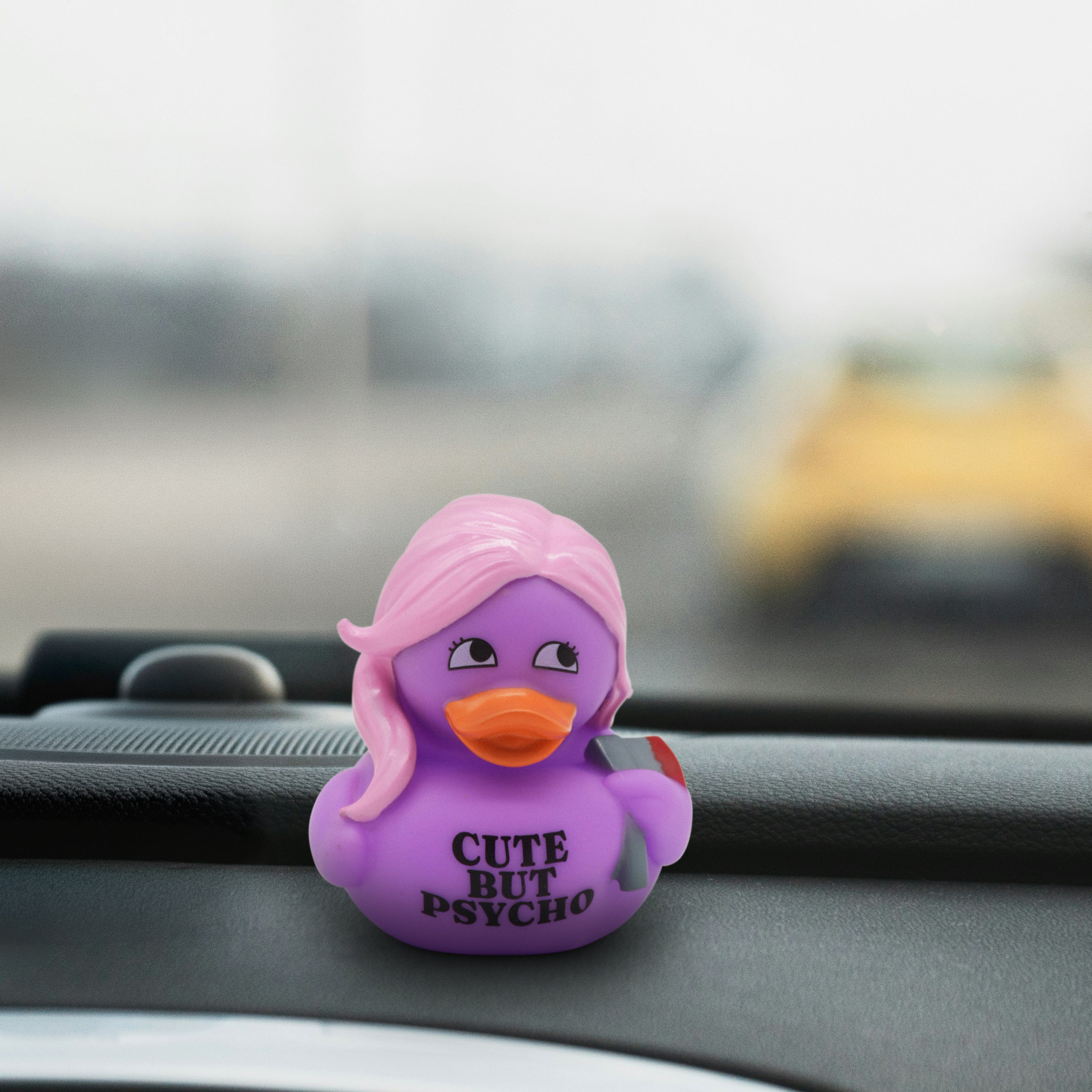 Purple duck-shaped car accessory that reads "cute but psycho" on a car dashboard.