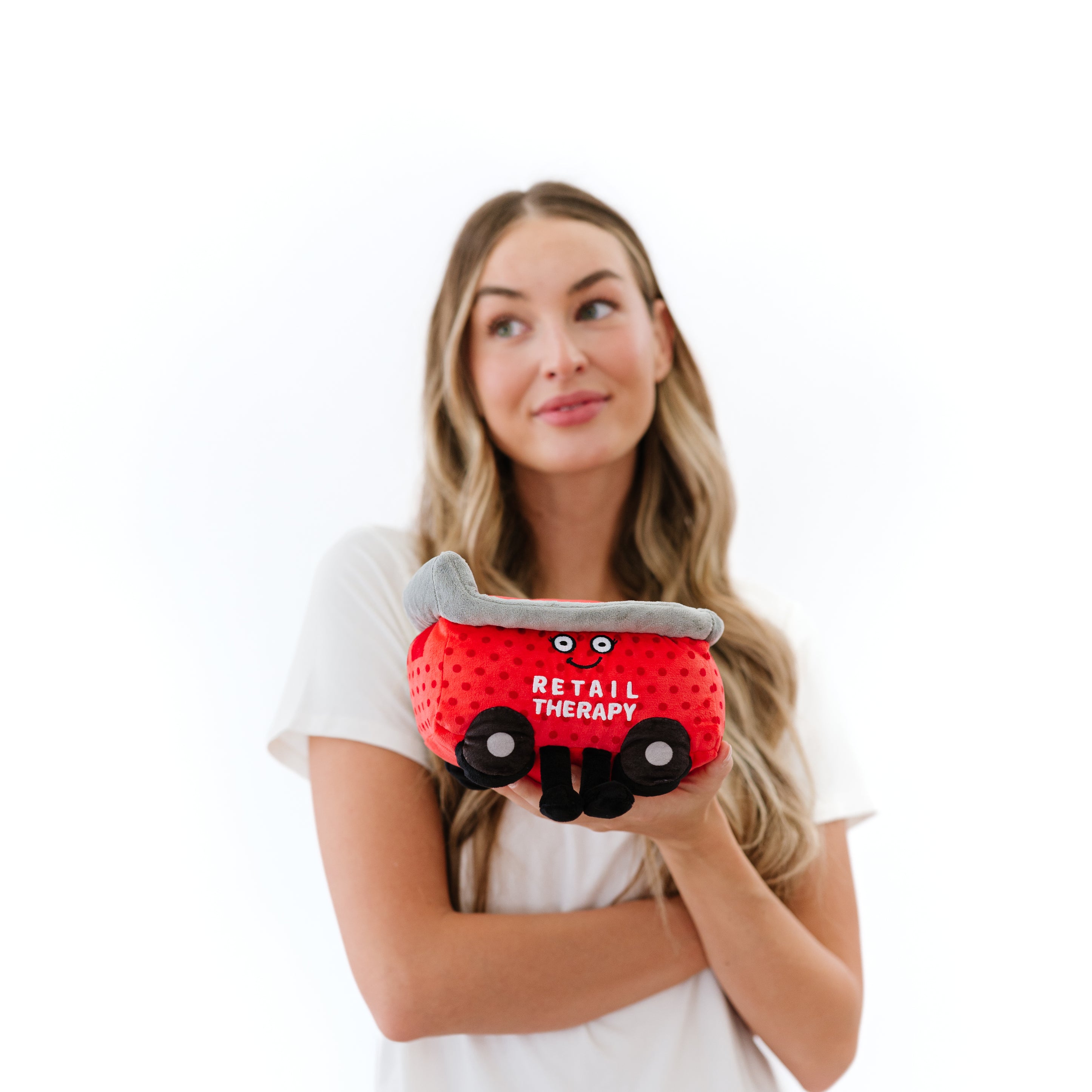 A model plush resembling a red shopping cart with the text 'RETAIL THERAPY' written on it, featuring a smiling face and black wheels.