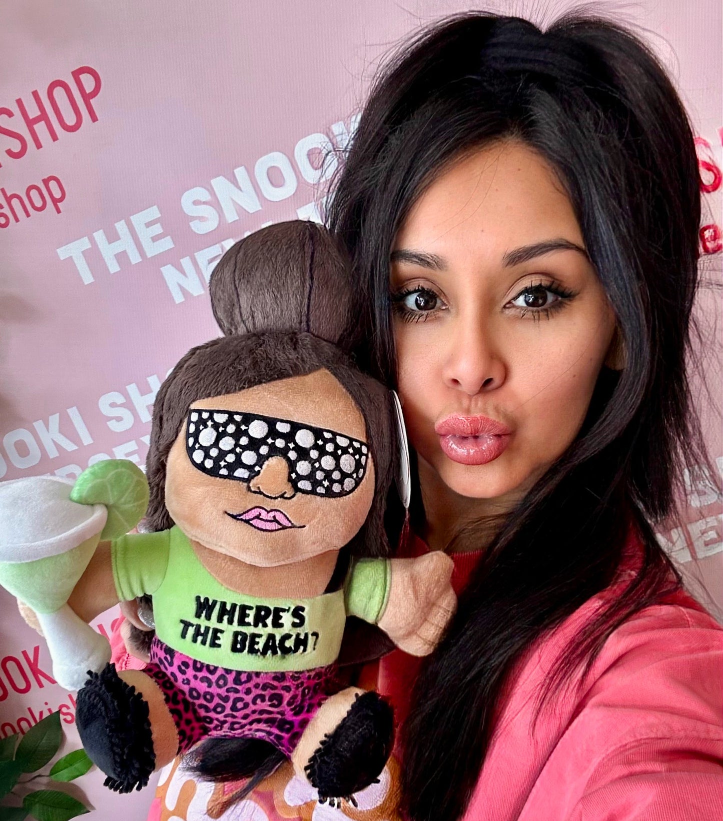Snooki holding a plush toy that's made to look like her wearing bedazzled sunglasses.