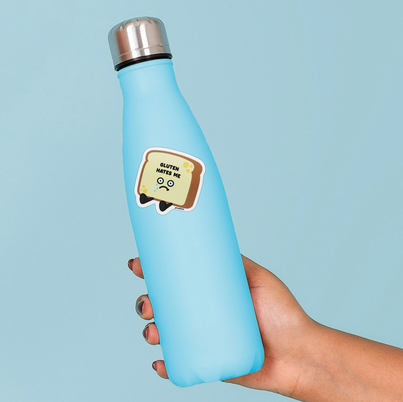 A light blue insulated water bottle with a silver cap, held in a hand against a solid light blue background. The bottle features a cute sticker of a sad slice of bread that says 'GLUTEN HATES ME'.
