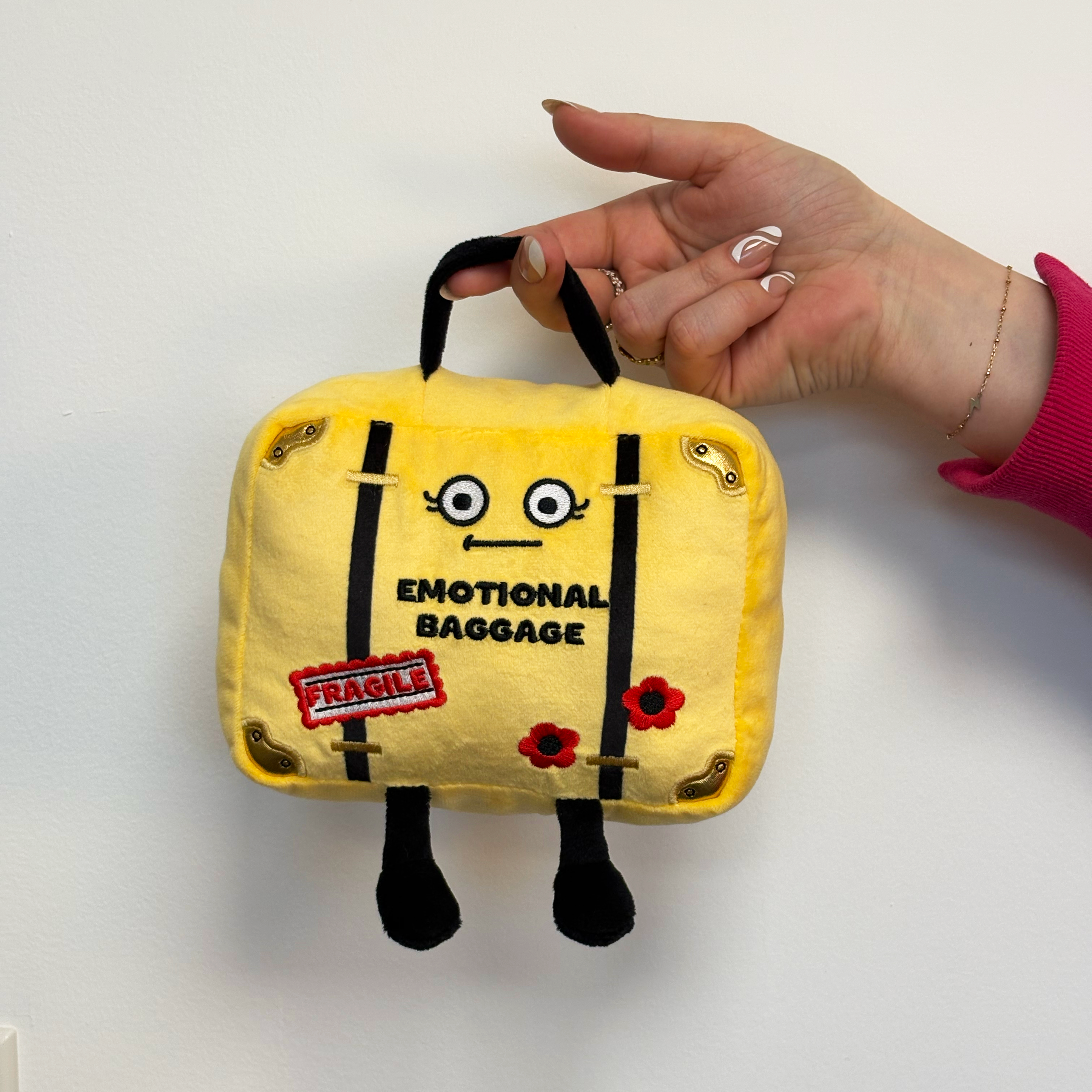 A hand holding a plush suitcase with a label that reads 'EMOTIONAL BAGGAGE.' 