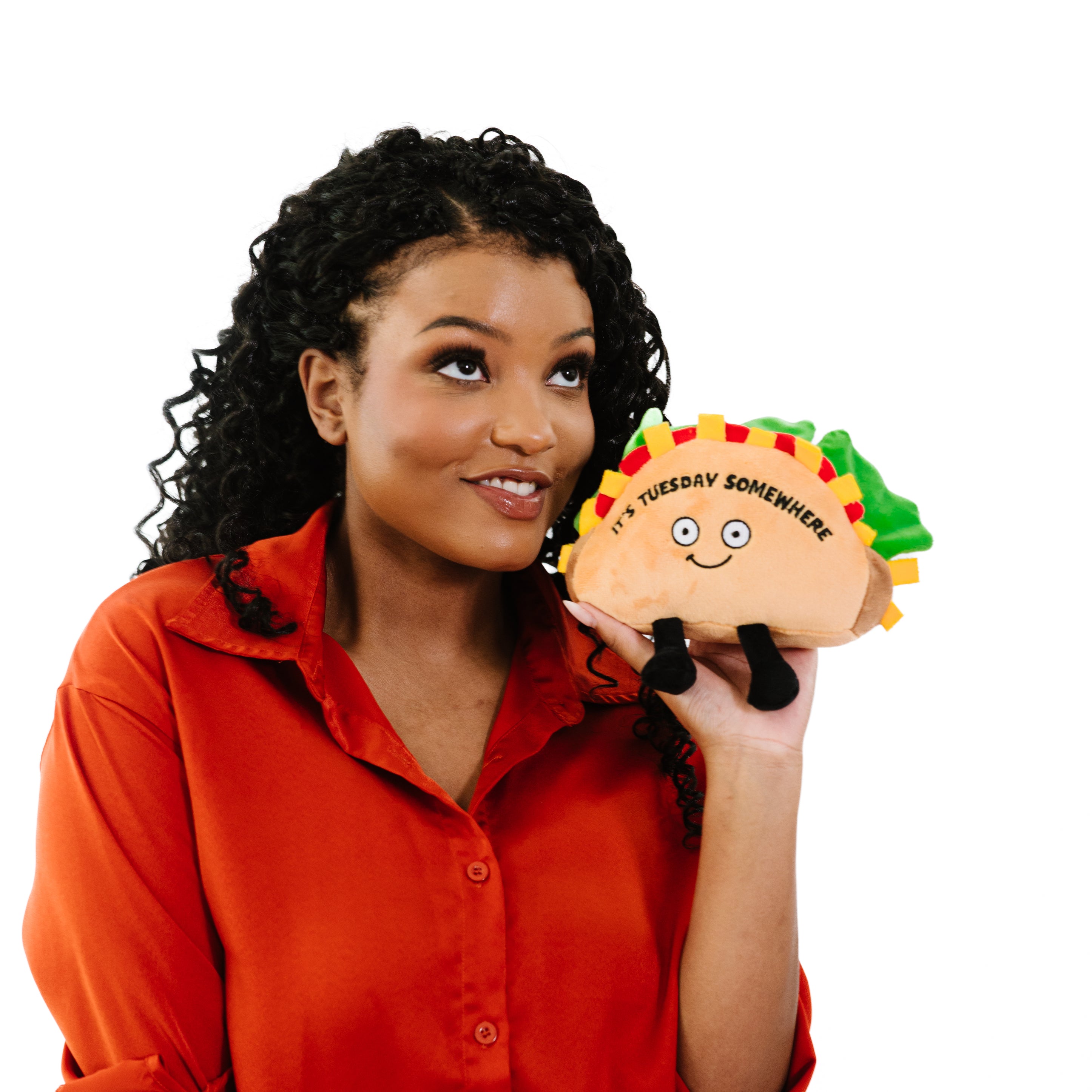 A woman holding  a plush shaped like a taco with a smiling face, green lettuce leaves, and the text 'IT'S TUESDAY SOMEWHERE' on the shell.