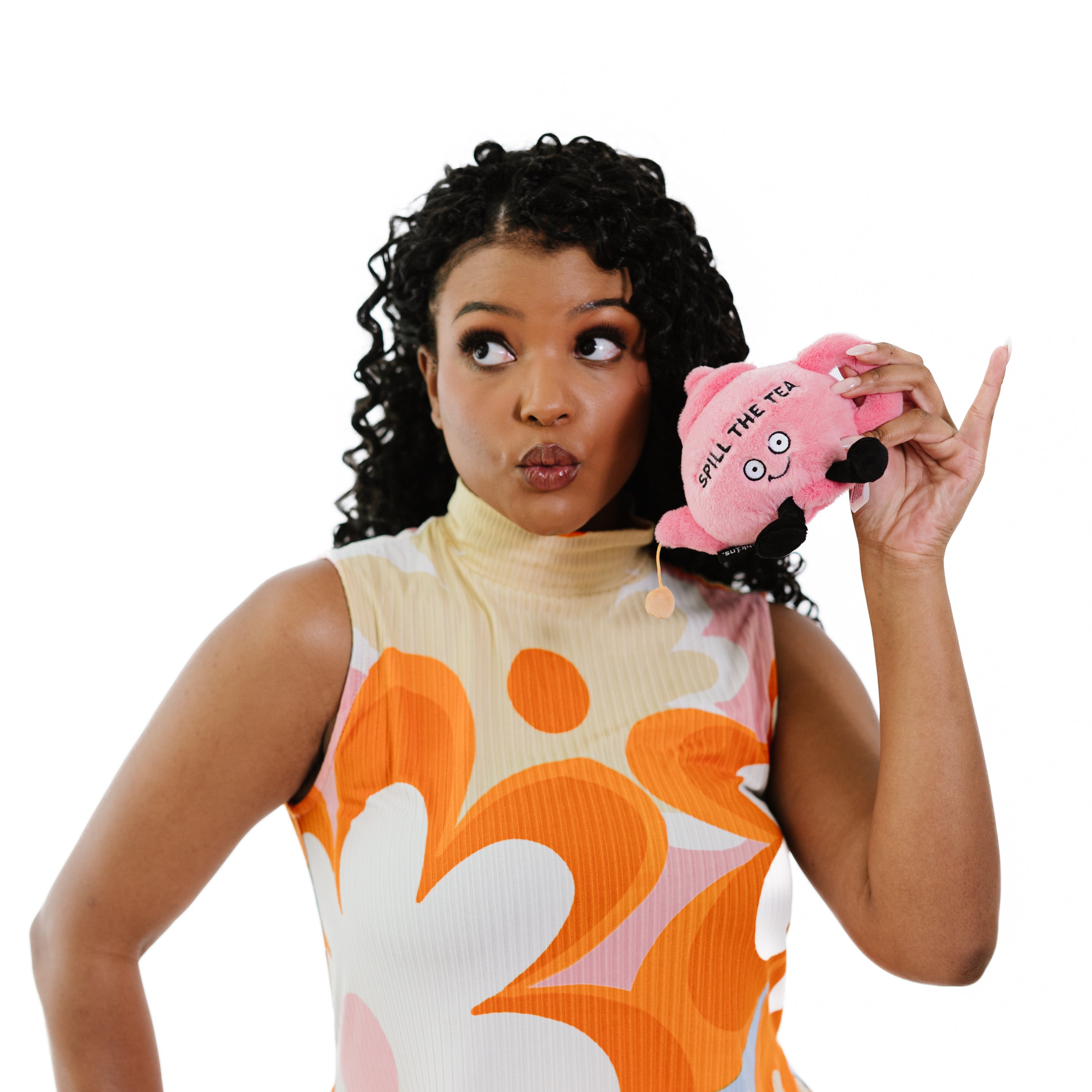 A woman holding a plush pink teapot with the phrase 'SPILL THE TEA' written on it .
