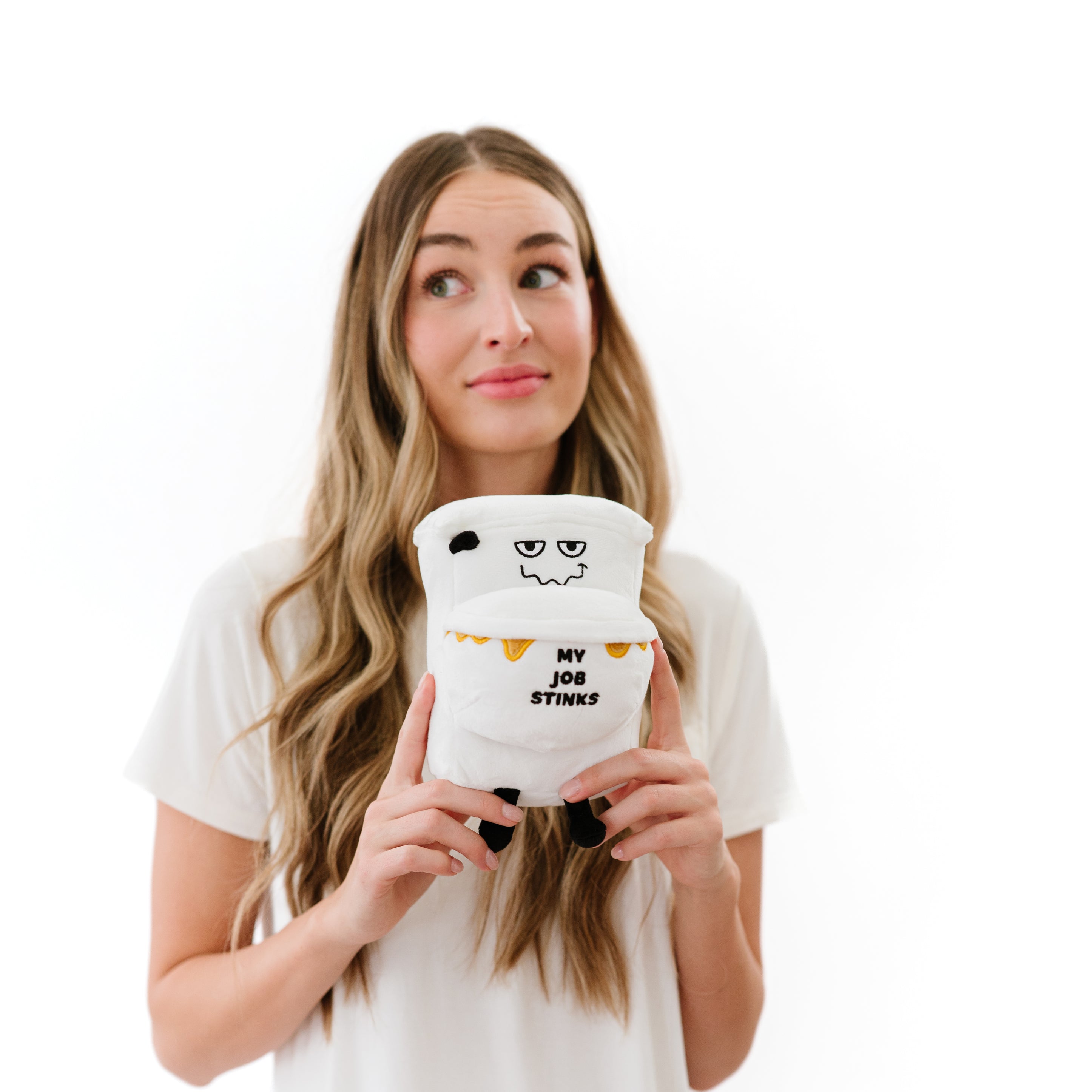 A woman holding a plush designed to resemble a dirty toilet with the text 'My job stinks' written on it.