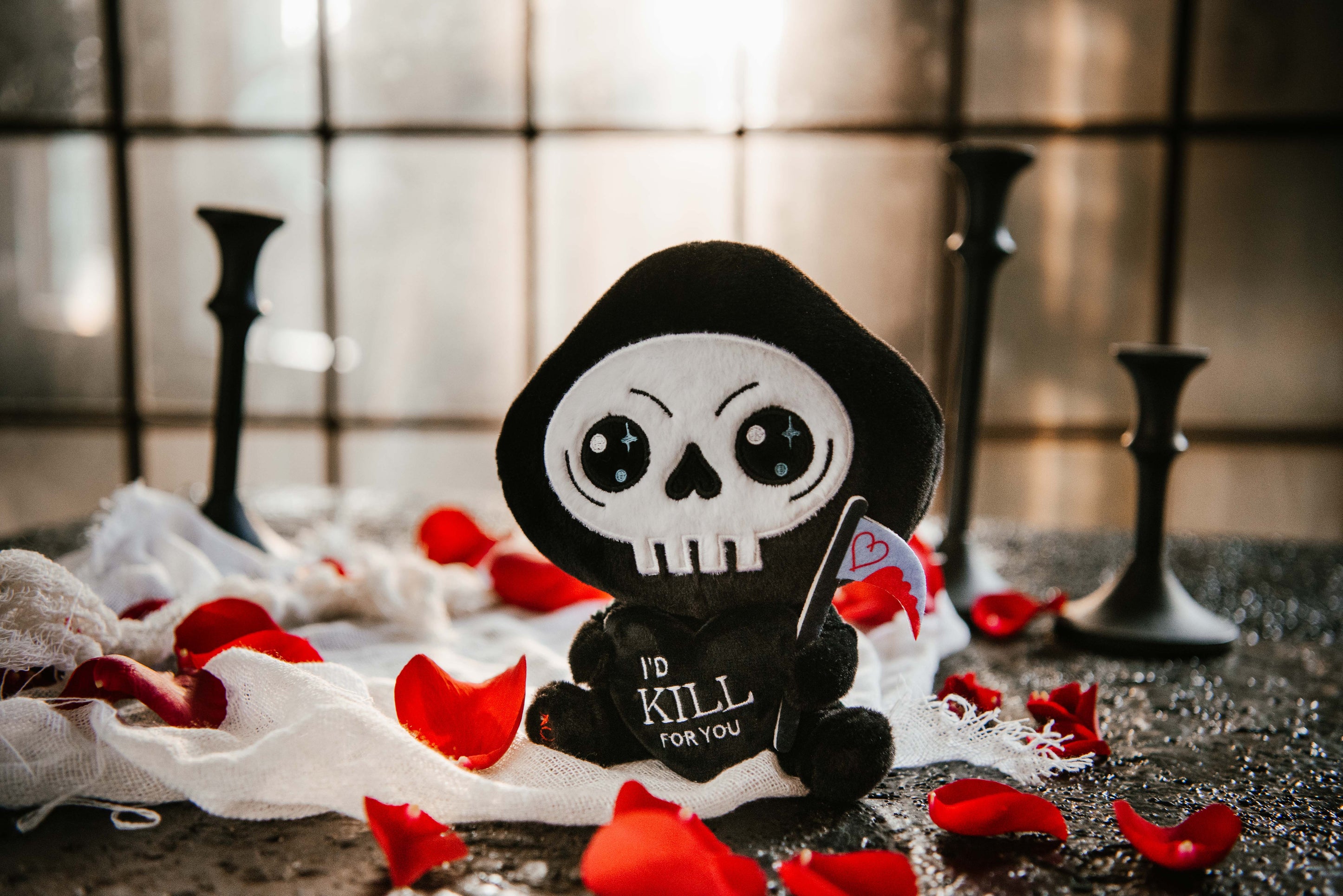 Grim reaper plush toy sitting on a bed of rose petals 