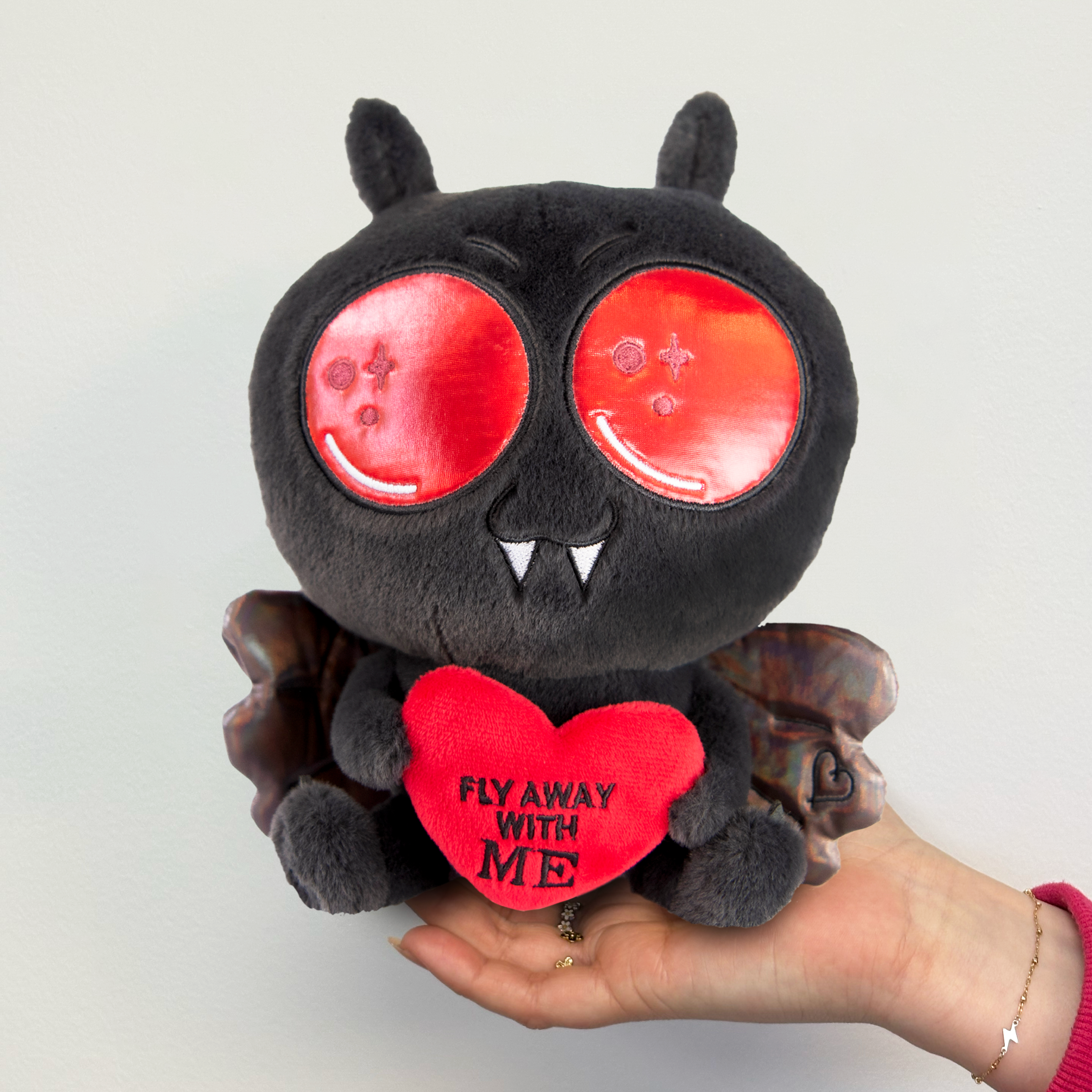 A hand holding a Mothman plushie that reads, "Fly away with me." 