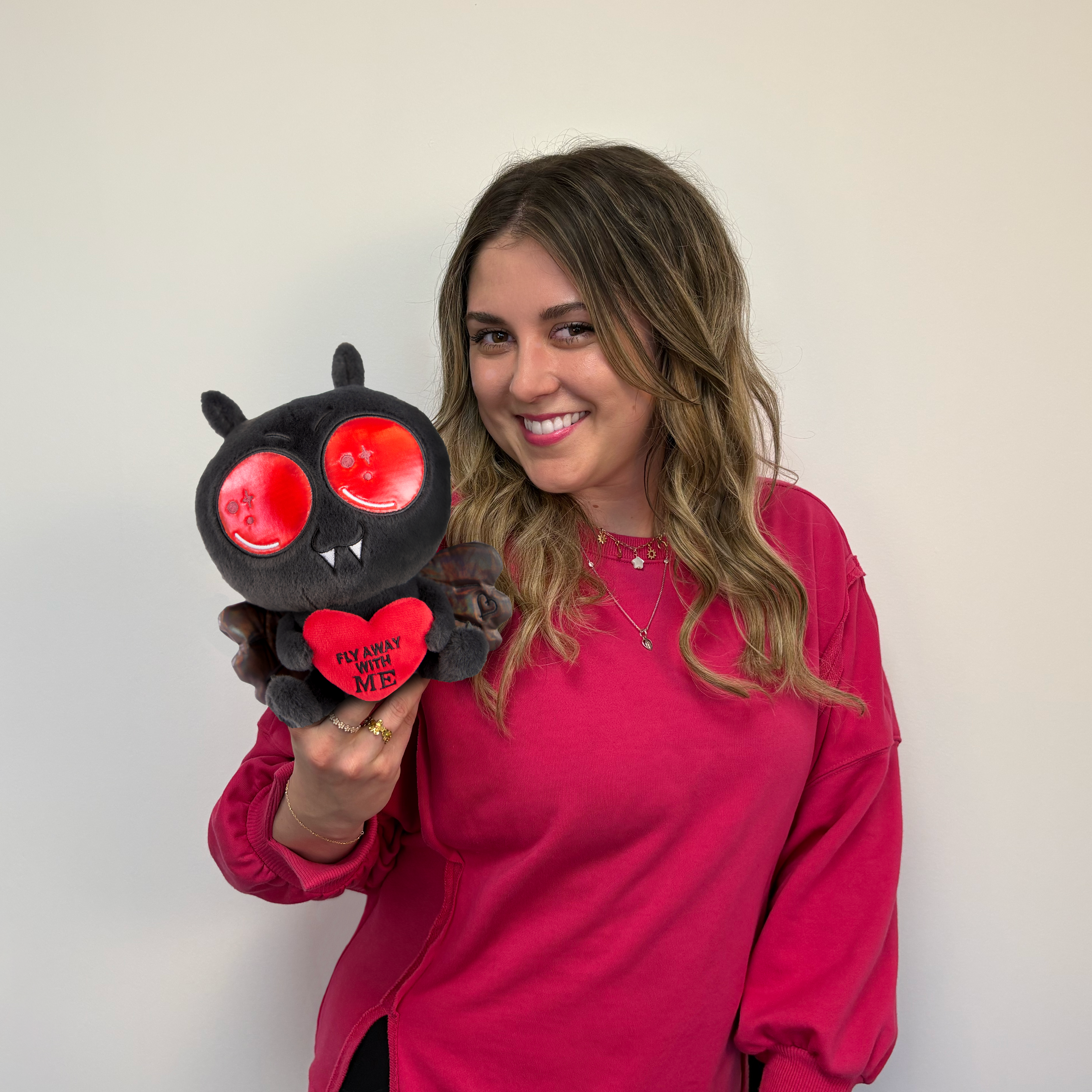 Woman holding a Mothman plushie that reads, "Fly away with me." 