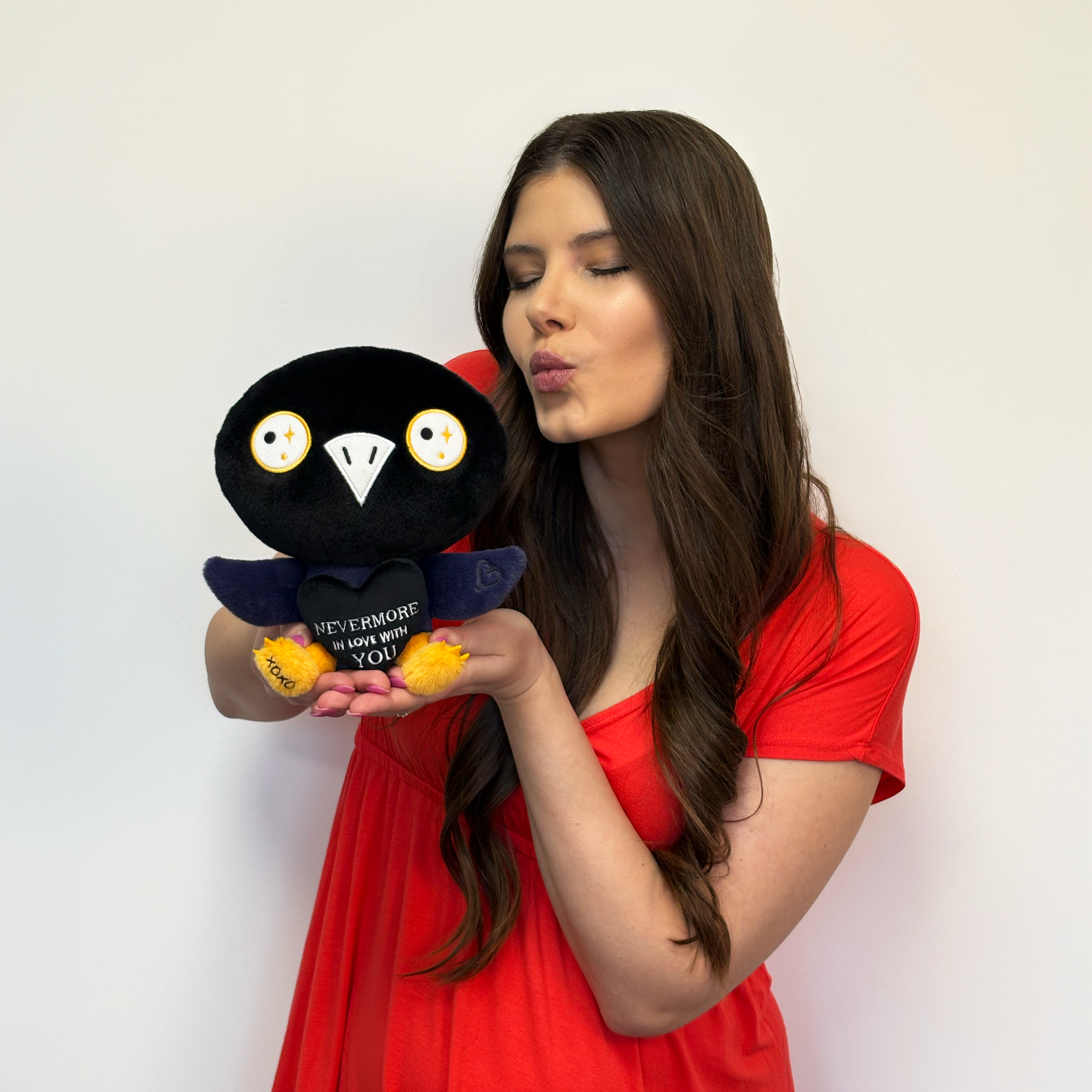Woman holding and blowing a kissy face at a raven plush toy that says, "Nevermore in love with you." 