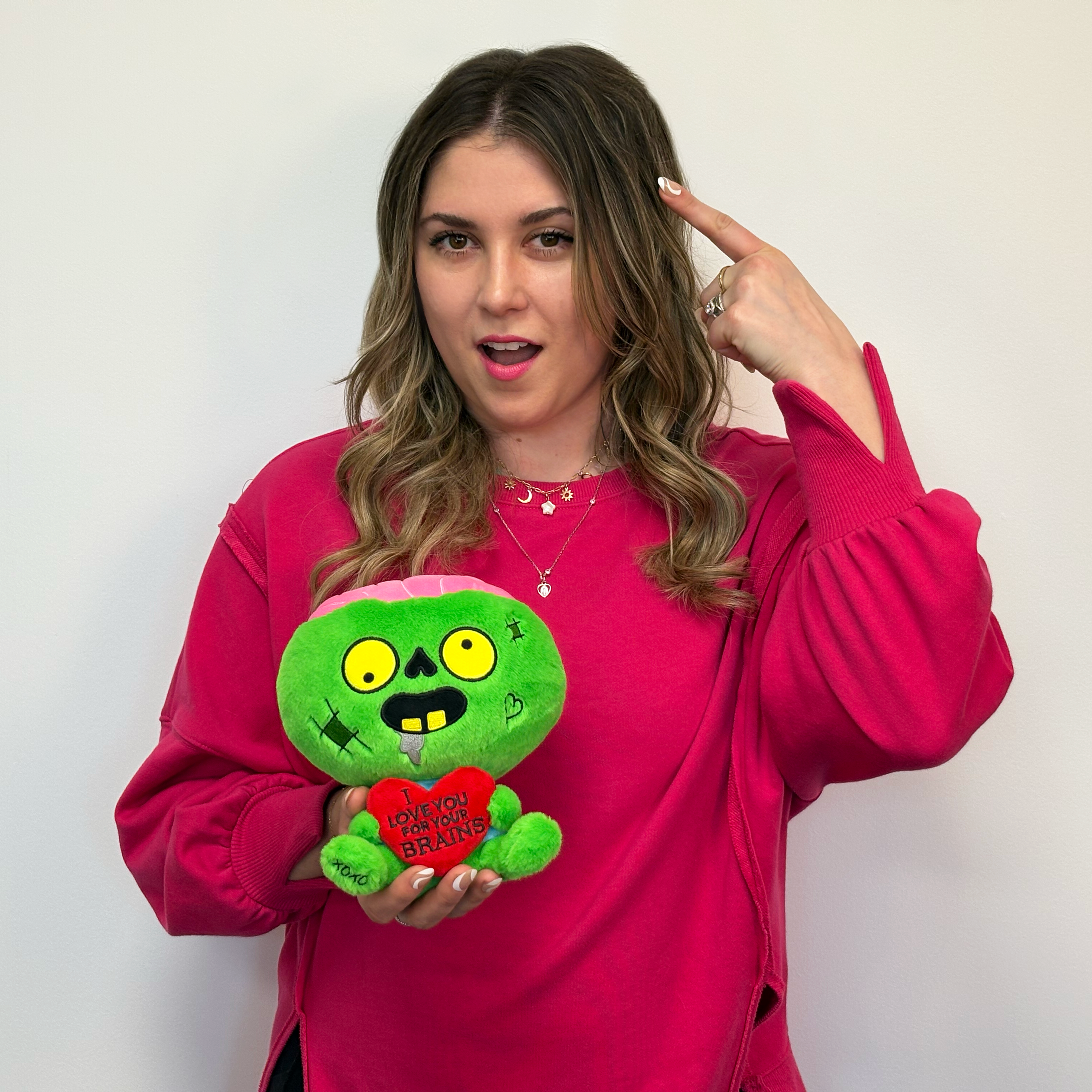 Woman holding a zombie plush with a 3D heart that reads, "I love you for your brains." 