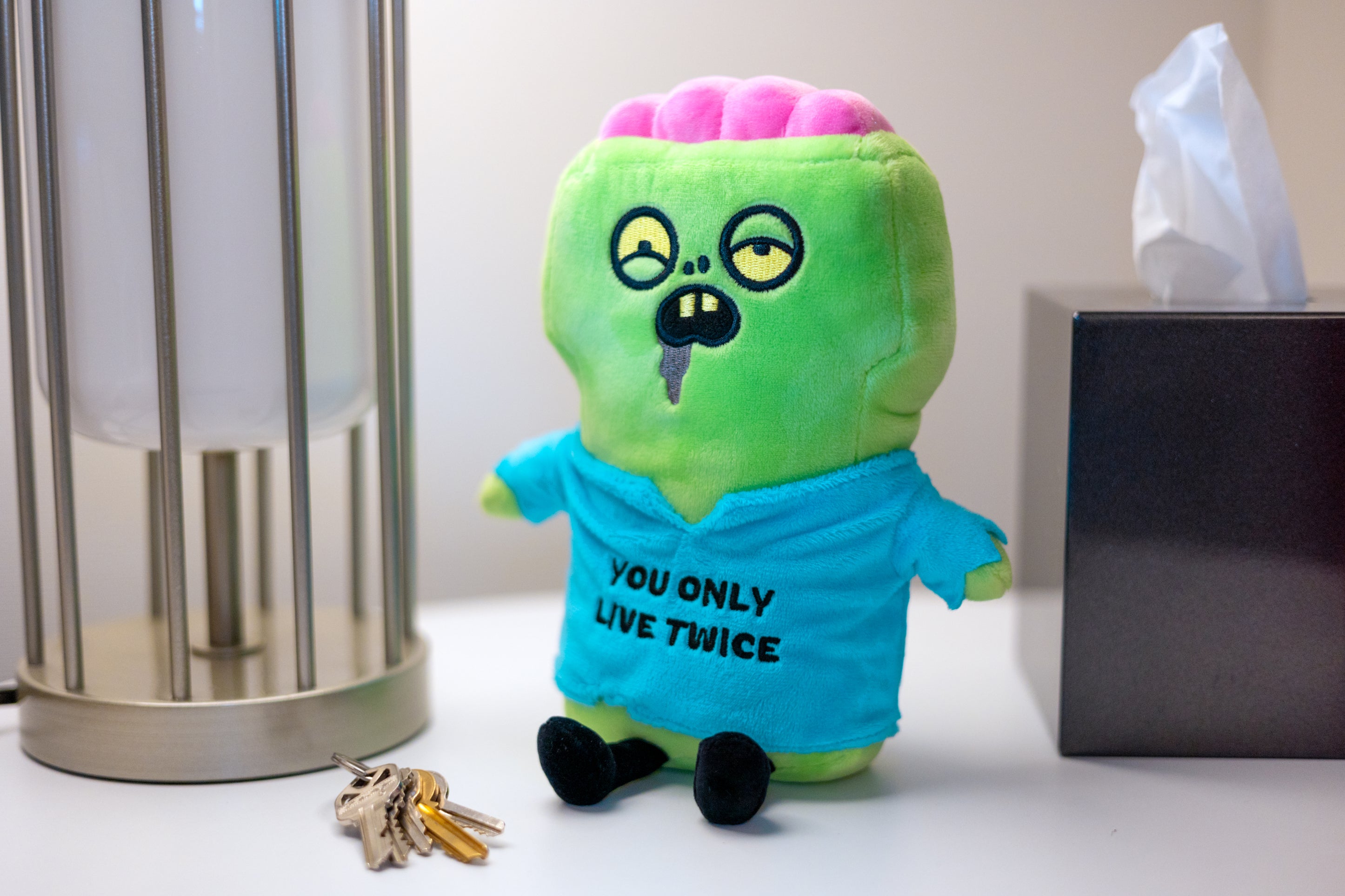 A plush depicting a cartoonish zombie wearing a blue shirt with the text 'YOU ONLY LIVE TWICE' placed on a dresser.